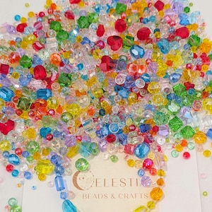 May include: A colourful collection of beads in a variety of shapes and sizes. The beads are a mix of red, blue, green, yellow, and clear, with some heart-shaped beads. A card with the text "CELESTIA BEADS & CRAFTS" is visible.