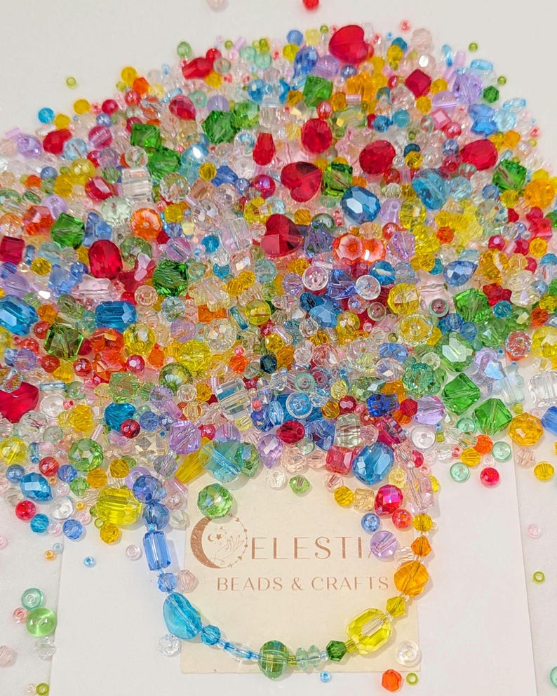 May include: A colourful collection of beads in a variety of shapes and sizes. The beads are a mix of red, blue, green, yellow, and clear, with some heart-shaped beads. A card with the text "CELESTIA BEADS & CRAFTS" is visible.