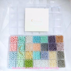 Peut inclure: Une bo&icirc;te de rangement en plastique transparent remplie de perles de fausses perles de diff&eacute;rentes couleurs. Les perles sont dispos&eacute;es dans des compartiments individuels. Une carte blanche avec le texte "Celestial Moon & Earth" est en haut &agrave; droite. Texte en bas : "Beads not included, for demo only".