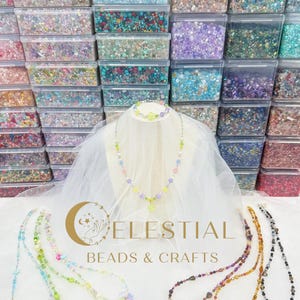 Peut inclure: Pr&eacute;sentation de colliers et bracelets de perles color&eacute;es, avec une vari&eacute;t&eacute; de couleurs et de motifs. Les colliers sont expos&eacute;s sur une surface blanche avec le texte "CELESTIAL BEADS & CRAFTS". En arri&egrave;re-plan, des rang&eacute;es de bo&icirc;tes en plastique transparent remplies de perles.