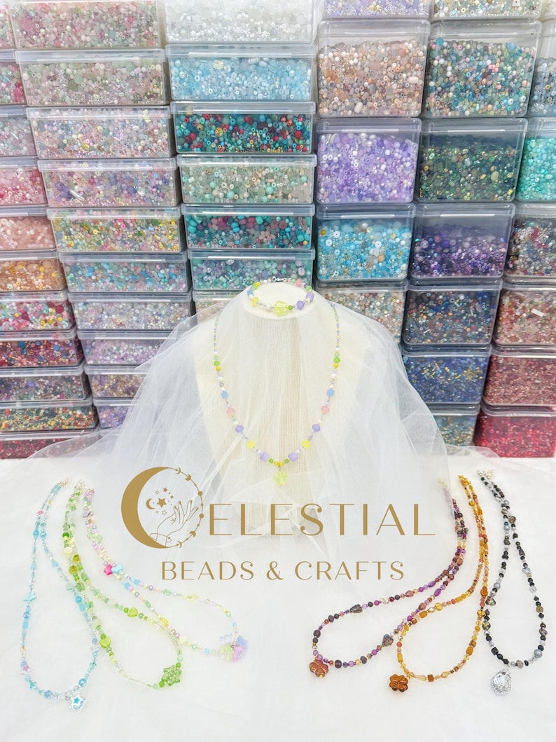 Peut inclure: Pr&eacute;sentation de colliers et bracelets de perles color&eacute;es, avec une vari&eacute;t&eacute; de couleurs et de motifs. Les colliers sont expos&eacute;s sur une surface blanche avec le texte "CELESTIAL BEADS & CRAFTS". En arri&egrave;re-plan, des rang&eacute;es de bo&icirc;tes en plastique transparent remplies de perles.