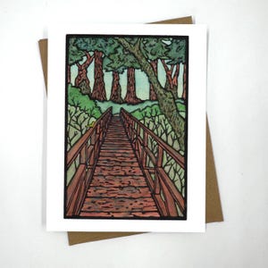 Może przedstawiać: Aquarela przedstawiająca drewniany most prowadzący do lasu. Most jest zbudowany z brązowych drewnianych desek i ma drewniane poręcze. Las składa się z wysokich zielonych drzew z niebieskim niebem w tle.