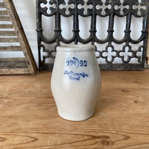 Könnte beinhalten: Ein beigefarbener Steingutkrug mit bauchigem Körper und schmalem Rand. Auf der Vorderseite befindet sich eine blaue Tintenaufschrift mit der Zahl 1790 und dem kursiven Schriftzug Van Dierenteyn Gent. Das Gefäß hat eine matte Oberfläche und Form.