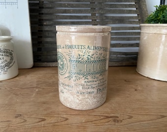 May include: A vintage ceramic jar with a cream-colored background and green floral design. The jar has a label that reads "F. Luce, Maison de Vente, 47, Rue de la Banque de l'Epargne, 43, Rue du 89, Place Clichy, Paris".