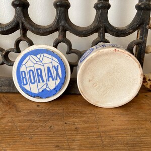 May include: An antique ceramic Borax container with a blue and white design. The lid features the word "BORAX" in a bold font, surrounded by a blue border. The container is off-white with a cracked texture.