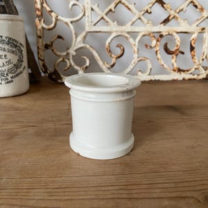 Könnte beinhalten: Weiße Keramikdose mit abgerundeter Oberseite und leicht ausgestelltem Boden. Die Dose hat eine glatte, matte Oberfläche.