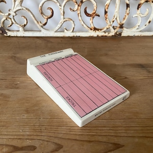 Puede incluir: Una tarjeta blanca con una cuadrícula rosa para llevar la puntuación del juego "The Kingsway". La tarjeta tiene las palabras "Tricks", "Honours", "Perpetual Bridge", "We First", "We Second", "Score" y "British Manufactures Ltd."