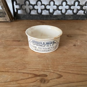 Può includere: Un piccolo vasetto rotondo in ceramica color bianco sporco con un'etichetta stampata in nero che riporta la scritta HORROCKS & WATSON SPRINGFIELD HOME POTTED MEATS SOUTHPORT. Il contenitore presenta un bordo svasato e segni di usura.