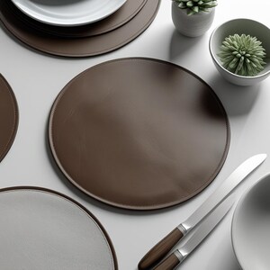 May include: A collection of brown and white leather placemats, with a stitched edge, arranged on a white surface. Two knives with wooden handles and a small white bowl with a green succulent are also present. The placemats are round.