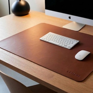 May include: A brown leather desk mat with a white keyboard and mouse. The mat has the word "LEDERI" embossed on the bottom right corner. A black sphere-shaped object sits on the desk in the background.