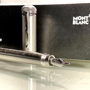 Peut inclure: Un stylo plume argent&eacute; avec un &eacute;tui et un capuchon assortis. Le stylo est pr&eacute;sent&eacute; sans le capuchon, r&eacute;v&eacute;lant la plume. L'&eacute;tui est noir avec le logo Montblanc. Instrument d'&eacute;criture de luxe.