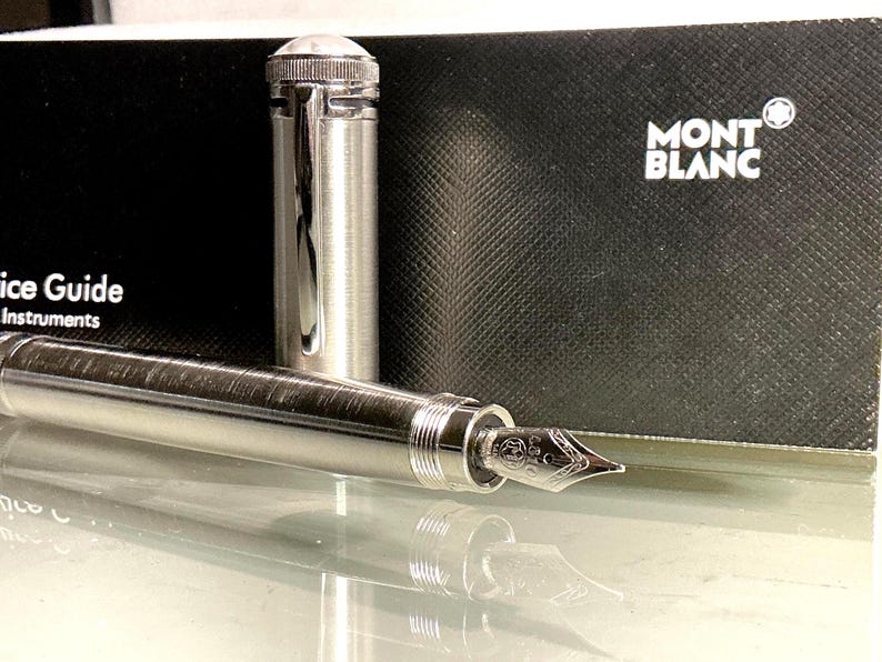 Peut inclure: Un stylo plume argent&eacute; avec un &eacute;tui et un capuchon assortis. Le stylo est pr&eacute;sent&eacute; sans le capuchon, r&eacute;v&eacute;lant la plume. L'&eacute;tui est noir avec le logo Montblanc. Instrument d'&eacute;criture de luxe.