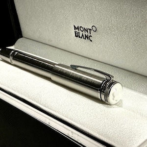 Peut inclure: Un stylo Montblanc argent&eacute; est pr&eacute;sent&eacute; dans un coffret noir avec un int&eacute;rieur blanc. Le stylo a une finition m&eacute;tallique brillante, un clip et un embl&egrave;me blanc. Le logo Montblanc est visible sur le coffret.