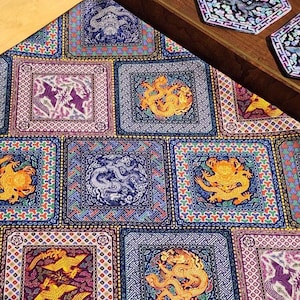 Puede incluir: Una tela estampada con diseños cuadrados repetidos con dragones y otros símbolos ornamentados en tonos azules, dorados y morados. Dos posavasos hexagonales con diseños de dragones están sobre una bandeja de madera.
