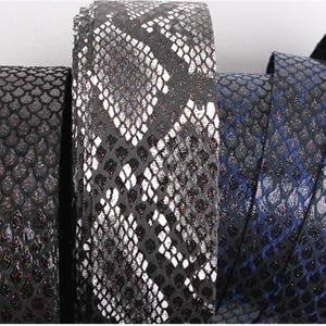 May include: Close-up of three rolled neckties with a reptile scale pattern. The ties are in shades of black, white, and blue. The fabric has a textured, shimmering appearance, suggesting a formal or luxury design.