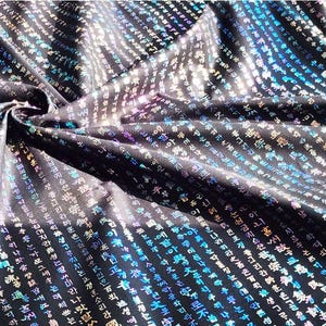 May include: Black fabric with a shimmering, iridescent sheen. The fabric is covered in a pattern of vertical rows of white and colored characters. The fabric is gathered in a swirl, creating folds and shadows.
