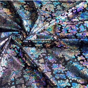 May include: Black fabric with a floral pattern. The flowers are in shades of blue, purple, and silver, with a metallic sheen. The fabric is gathered, creating folds and shadows.
