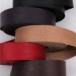May include: A selection of coiled ribbon in shades of black, dark purple, tan, red, and dark brown. Each ribbon displays a textured, snake-skin-like pattern. These ribbons are suitable for crafting or decorative applications, and are likely sold by the meter.