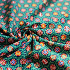 Puede incluir: Primer plano de una tela verde con un patrón repetitivo de diseños circulares rojos, azules, amarillos y blancos. La tela tiene un fondo geométrico y está doblada, mostrando la textura y profundidad del material.