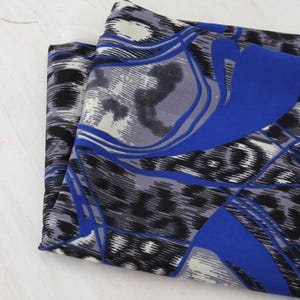 May include: Folded fabric with a bold pattern featuring black, gray, and white leopard print, accented with vibrant blue geometric shapes. The fabric is layered, showcasing the design's repeating elements.