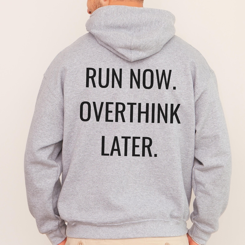 May include: A light gray hoodie with the text "RUN NOW. OVERTHINK LATER." printed in black block letters across the back. The hoodie has a hood and long sleeves. The person wearing the hoodie is facing away from the camera.