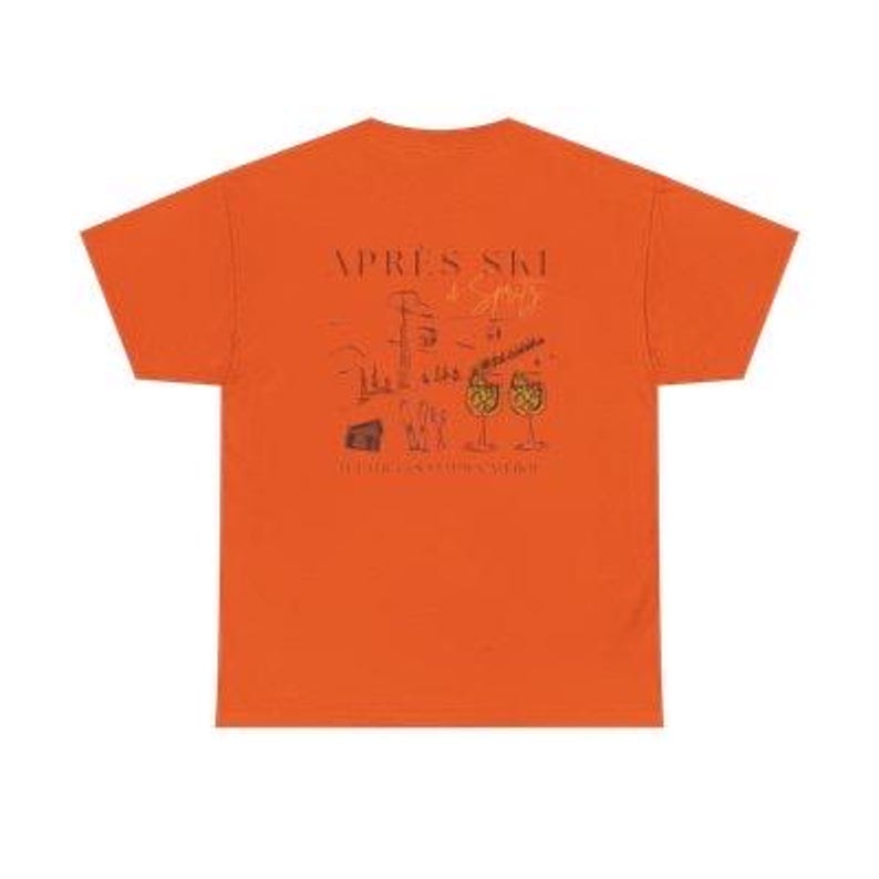 May include: Orange t-shirt with a graphic design on the back. The design includes the words "APRES SKI" above a sketch of a mountain scene, cocktails, and the phrase "IT'S ALWAYS COCKTAIL HOUR".