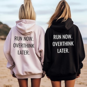 May include: Two hooded sweatshirts, one light pink and one black, with the text "RUN NOW. OVERTHINK LATER." printed in white on the back. The sweatshirts are worn by two people standing on a beach.