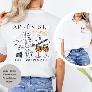 May include: White unisex t-shirt with a graphic design featuring the text "APR&Egrave;S SKI & Spritz" above a mountain scene with ski lifts and two Aperol Spritz cocktails. The phrase "LET THE GOOD TIMES APEROL" is below the graphic.