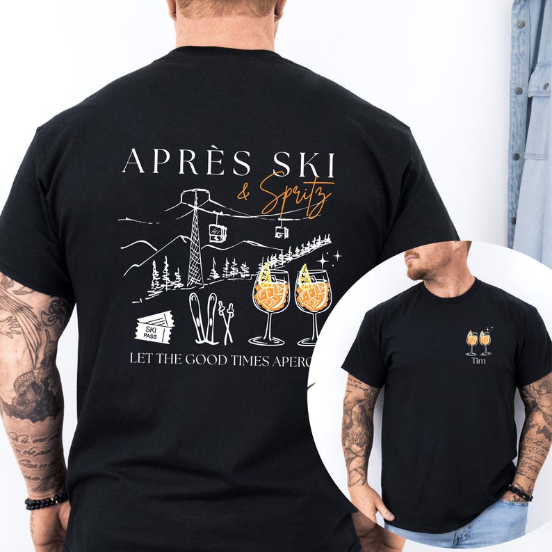 May include: Black t-shirt with a white and orange graphic design. The design includes the text "APR&Egrave;S SKI & Spritz" above a mountain scene with ski lifts, skis, and two cocktail glasses. The text "LET THE GOOD TIMES APER" is below the graphic.