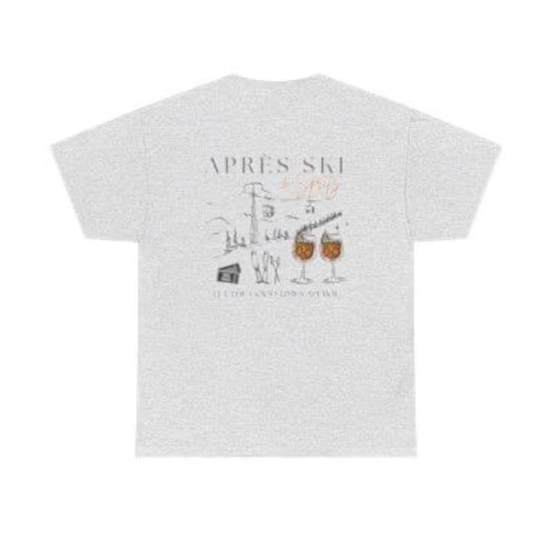 May include: A light gray t-shirt with a graphic design on the back. The design features the words "Apr&egrave;s Ski" above a drawing of a ski resort scene with two cocktails. The text "It's for relaxation time" is below the drawing.