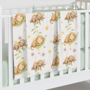 Peut inclure: Une couverture pour bébé blanche avec un motif répétitif de paresseux brun clair dormant sur des feuilles et des branches vertes, agrémenté de petites fleurs jaunes, de vignes vertes et de minuscules colibris. Le style est aquarellé.