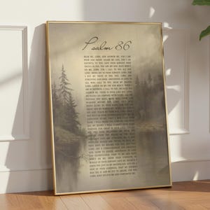 Könnte beinhalten: Ein gerahmter Druck von Psalm 86, der eine ruhige Landschaft mit einem See und Bäumen zeigt. Der Text des Psalms wird vertikal angezeigt, mit dem Titel oben. Der Rahmen ist goldfarben, und der Druck lehnt an einer Wand.