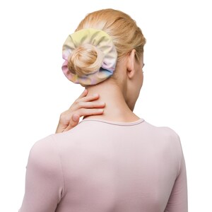 May include: A pastel-colored scrunchie wrapped around a bun hairstyle. The scrunchie features a soft blend of yellow, pink, and blue hues. The person is wearing a light pink long-sleeved shirt.