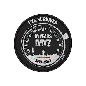 Könnte beinhalten: Ein schwarz-weißer runder Aufnäher mit dem Text "I'VE SURVIVED" oben. Der Aufnäher zeigt ein Messgerätdesign mit "10 YEARS DAYZ" in der Mitte und "2013-2023" unten. Unter dem Text befindet sich eine rote Linie.