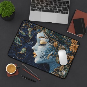 May include: A blue and gold mousepad with an embroidered design of a woman's face with her eyes closed. The woman's face is surrounded by flowers and leaves.