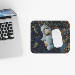 May include: A blue and gold embroidered mouse pad featuring a woman's face with her eyes closed. The woman's hair is adorned with gold and green embroidery.