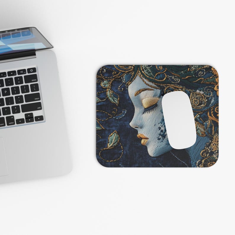 May include: A blue and gold embroidered mouse pad featuring a woman's face with her eyes closed. The woman's hair is adorned with gold and green embroidery.
