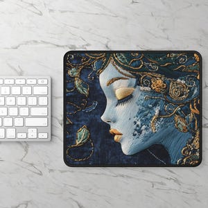 May include: A blue and gold embroidered mouse pad featuring a woman's face with her eyes closed. The woman's face is surrounded by intricate floral designs.