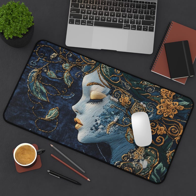 May include: A blue and gold embroidered mouse pad featuring a woman's face with her eyes closed. The woman's face is surrounded by intricate floral designs.