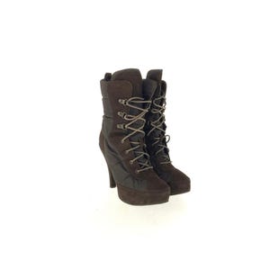 May include: A pair of brown high-heeled boots with a lace-up design. The boots have a platform sole and a high heel. The upper part of the boots is made of a quilted material, and the laces are a light brown color.