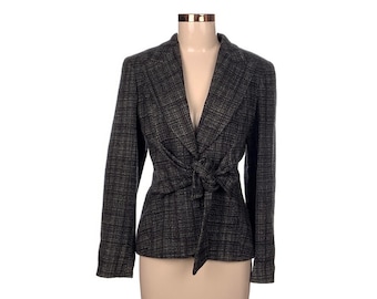 Puede incluir: Un blazer a cuadros grises y negros con cierre de lazo. El blazer tiene mangas largas y solapas con muescas. La chaqueta se exhibe en un maniquí sobre un fondo blanco.