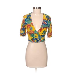 Puede incluir: Top envolvente amarillo con estampado tropical con palmeras, pi&ntilde;as y escenas oce&aacute;nicas. La parte superior tiene mangas cortas y un escote en V profundo. El dobladillo inferior est&aacute; recogido.