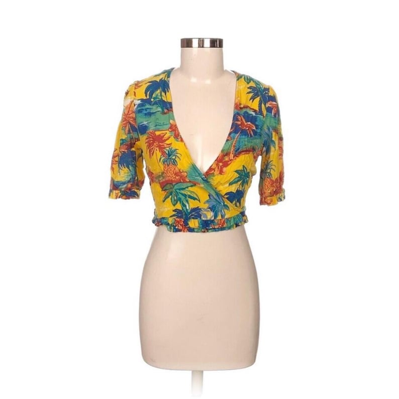 Puede incluir: Top envolvente amarillo con estampado tropical con palmeras, pi&ntilde;as y escenas oce&aacute;nicas. La parte superior tiene mangas cortas y un escote en V profundo. El dobladillo inferior est&aacute; recogido.