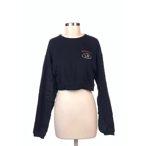 May include: Black cropped sweatshirt with long sleeves. The sweatshirt features the text "Joberg" in red above a white oval with the letters "LB" inside. The garment is displayed on a mannequin against a white background.