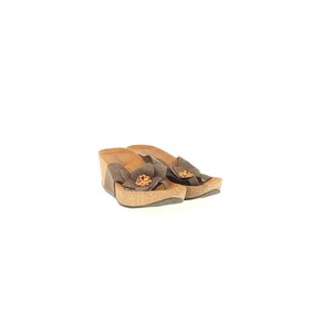 May include: A pair of brown wedge sandals with a flower accent on the toe. The sandals have a cork sole and a suede-like upper. The flower is a darker shade of brown, adding a decorative touch to the footwear.