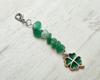 May include: A silver charm bracelet with a green four-leaf clover charm. The bracelet is made with green and white stones.