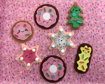 May include: Six felt Christmas ornaments in the shape of a star, a snowflake, a Christmas tree, and three donuts. The ornaments are decorated with sprinkles, glitter, and googly eyes.