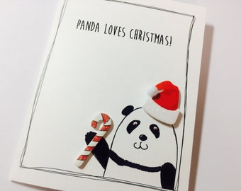 May include: A white card with black text that reads "Panda Loves Christmas!" A black and white panda illustration is on the card wearing a red and white Santa hat and holding a red and white candy cane.