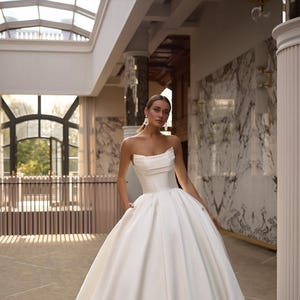 May include: A white strapless wedding dress with a fitted bodice and a full, flowing skirt. The dress is made of a smooth, satin fabric and has a simple, elegant design.