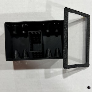 以下が含まれることがあります： 透明な蓋と複数のコンパートメントが付いた黒いプラスチック製の収納ボックス。ボックスの内側にはグリッドパターンがあり、小さなアイテムを収納するために設計されています。